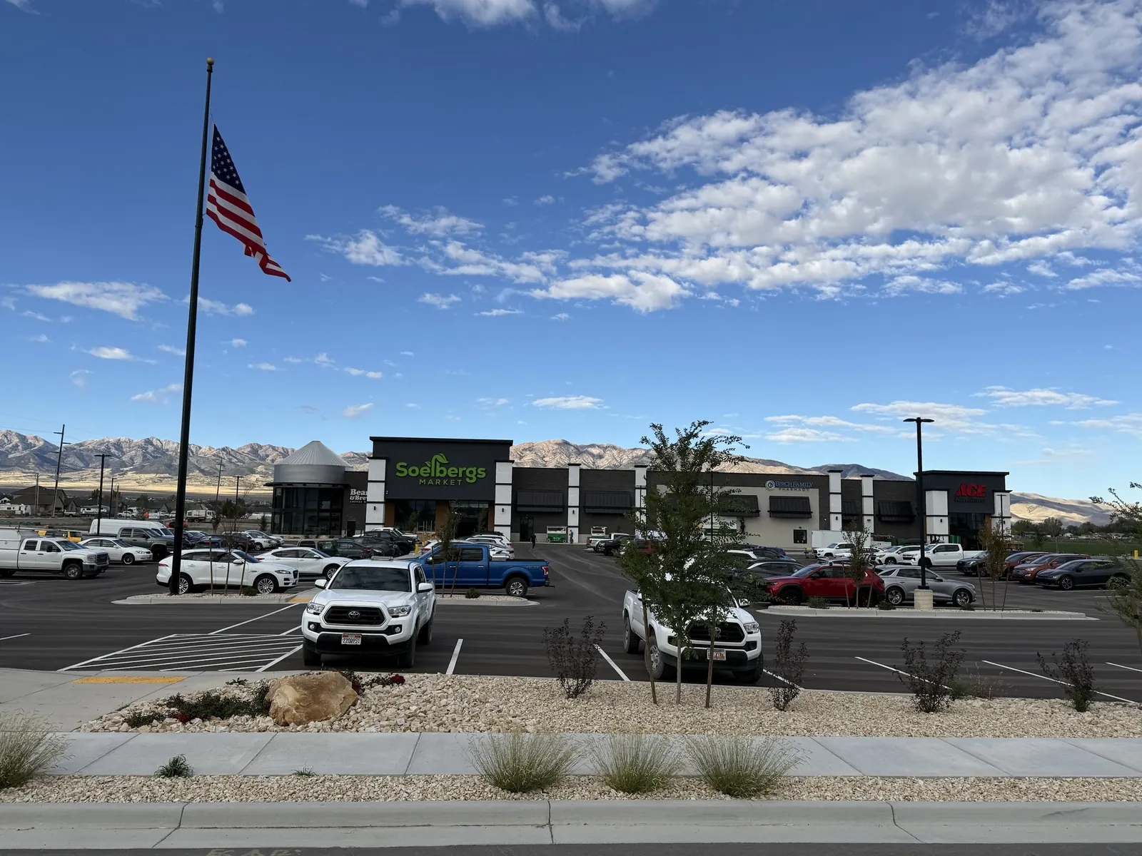 The full shopping center seen from the road, with an American flag and mountains behind it