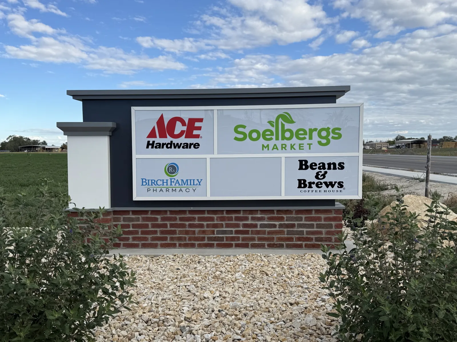 Monument sign with the Ace Hardware, Soelbergs Market, Birch Family Pharmacy and Beans & Brews logos